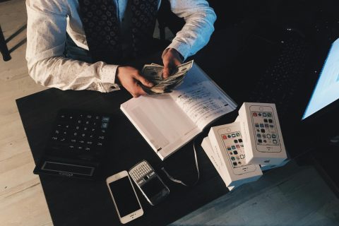 Businessman organizing finances with tech devices and cash on desk.